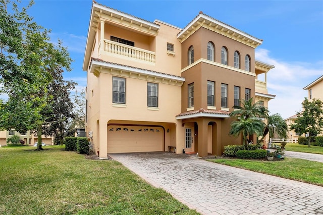 mediterranean / spanish-style home featuring an attached garage, a balcony, decorative driveway, stucco siding, and a front yard