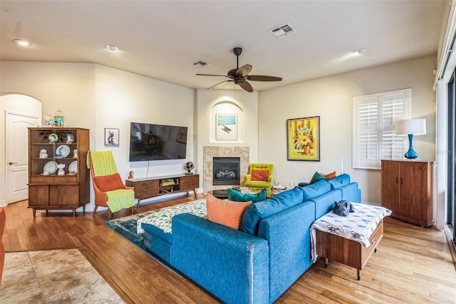 living area featuring a tiled fireplace, wood finished floors, visible vents, and a ceiling fan