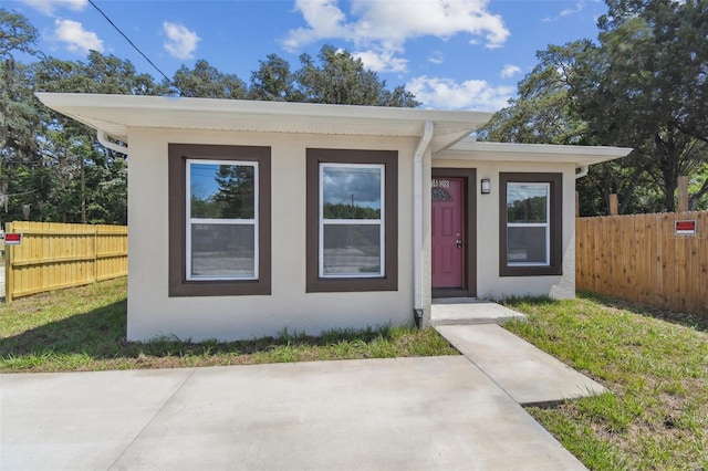 bungalow-style home featuring a front lawn, fence, and stucco siding