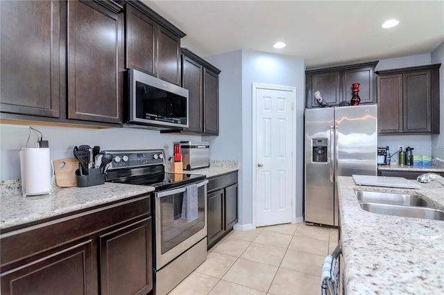 kitchen with appliances with stainless steel finishes, light tile patterned flooring, a sink, and dark brown cabinetry