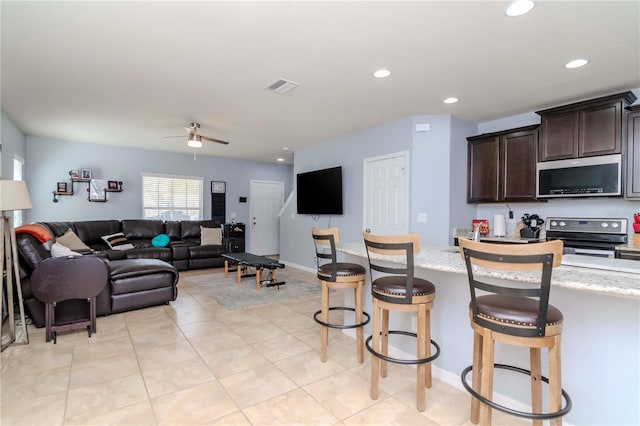 kitchen featuring appliances with stainless steel finishes, visible vents, dark brown cabinets, and light stone countertops