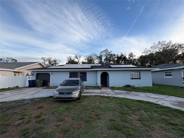 ranch-style home featuring concrete driveway, fence, a front lawn, and solar panels