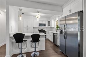 kitchen with appliances with stainless steel finishes, white cabinets, a peninsula, and a breakfast bar area