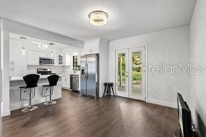 kitchen with stainless steel appliances, a breakfast bar, a peninsula, white cabinetry, and dark wood finished floors