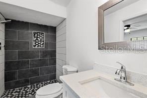 bathroom featuring ceiling fan, tiled shower, vanity, and toilet