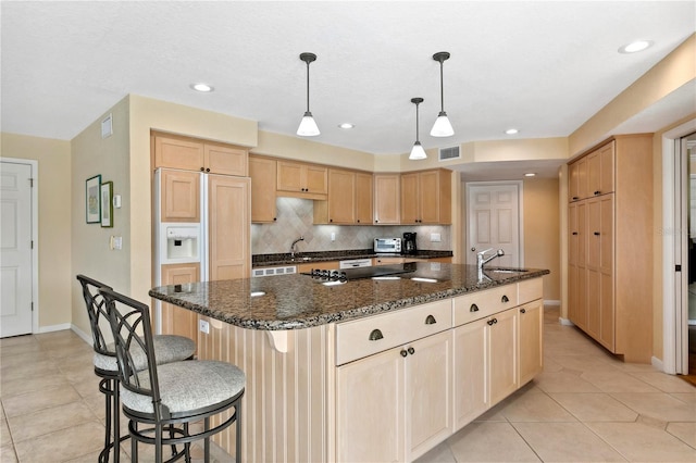 kitchen featuring a center island with sink, visible vents, backsplash, light brown cabinets, and a sink