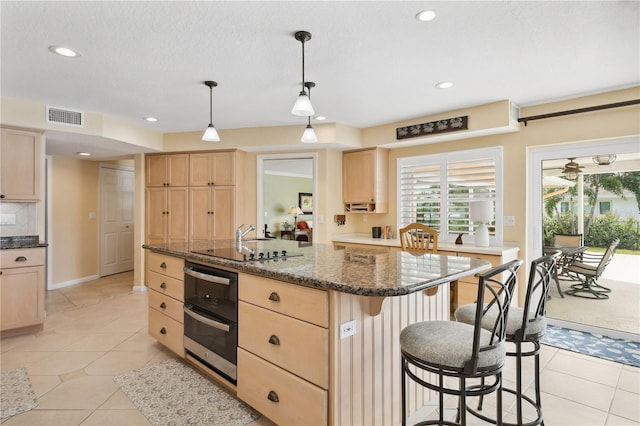 kitchen featuring a center island with sink, visible vents, a wealth of natural light, and light brown cabinetry