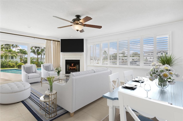 living room featuring a warm lit fireplace, ceiling fan, and light tile patterned flooring