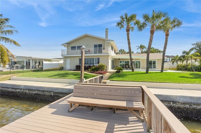 rear view of house featuring a balcony, a water view, fence, a yard, and stucco siding