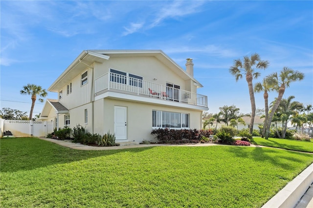 view of front facade featuring a front lawn, fence, a balcony, and stucco siding