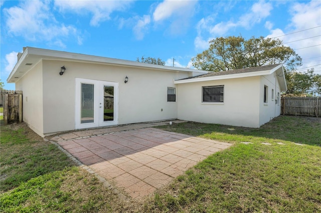 rear view of house with stucco siding, a lawn, a patio, fence, and french doors