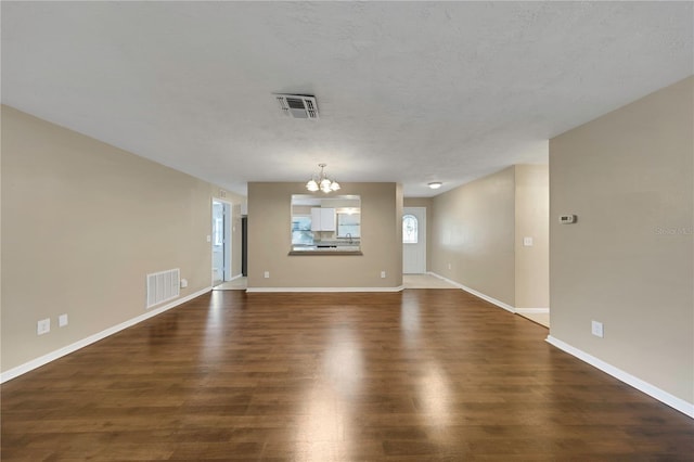 empty room featuring visible vents, baseboards, a chandelier, and dark wood-style flooring