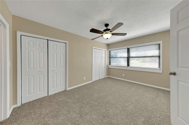 unfurnished bedroom with carpet flooring, ceiling fan, two closets, and baseboards