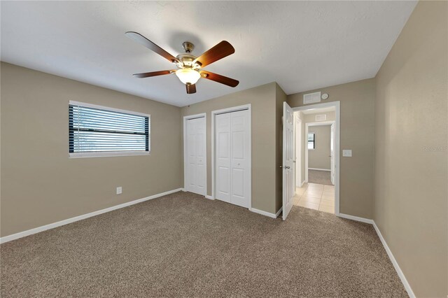 unfurnished bedroom featuring visible vents, two closets, baseboards, light colored carpet, and a ceiling fan