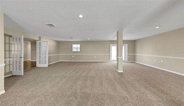 basement featuring visible vents, baseboards, french doors, a textured ceiling, and carpet flooring