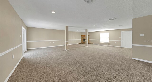 basement with visible vents, carpet, baseboards, a fireplace, and a textured ceiling