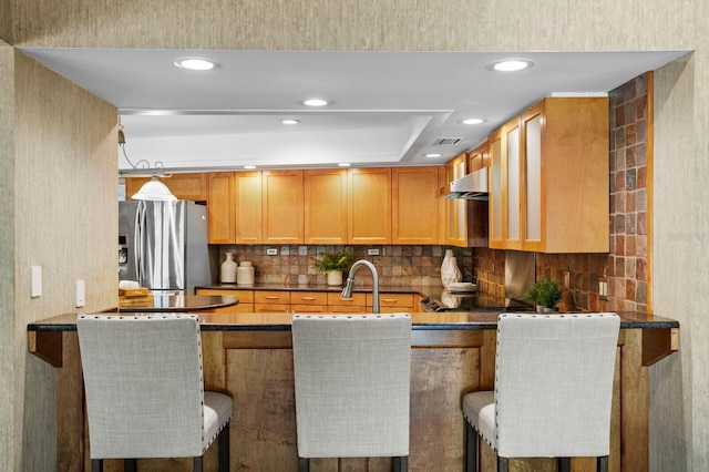 kitchen featuring dark countertops, backsplash, a peninsula, and stainless steel fridge with ice dispenser