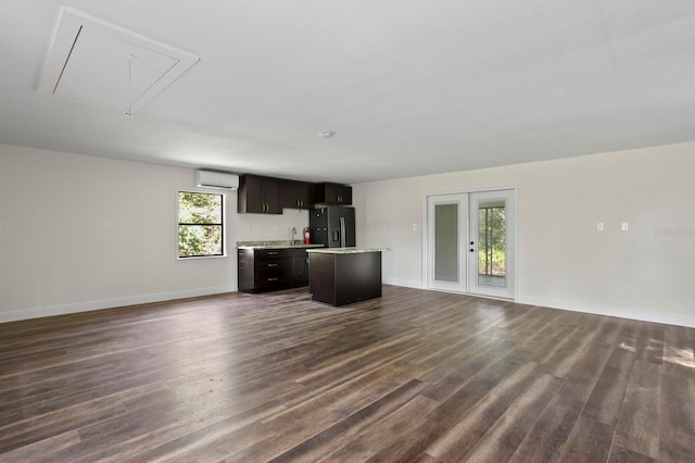 unfurnished living room with attic access, baseboards, dark wood finished floors, french doors, and a wall mounted AC