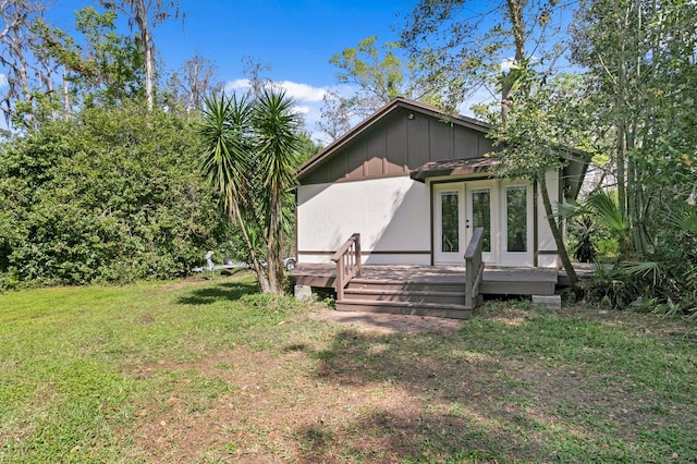 rear view of property with a deck, a yard, french doors, and board and batten siding