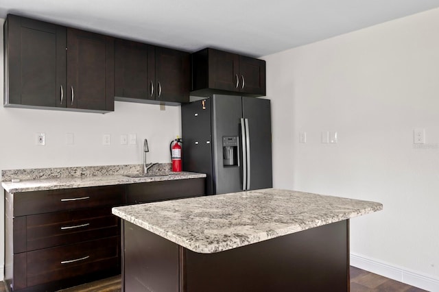 kitchen featuring dark brown cabinetry, baseboards, dark wood-type flooring, fridge with ice dispenser, and a sink