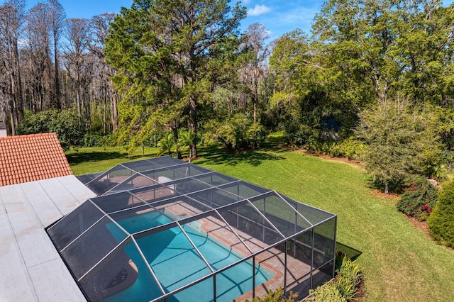 outdoor pool with glass enclosure, a view of trees, a lawn, and a patio