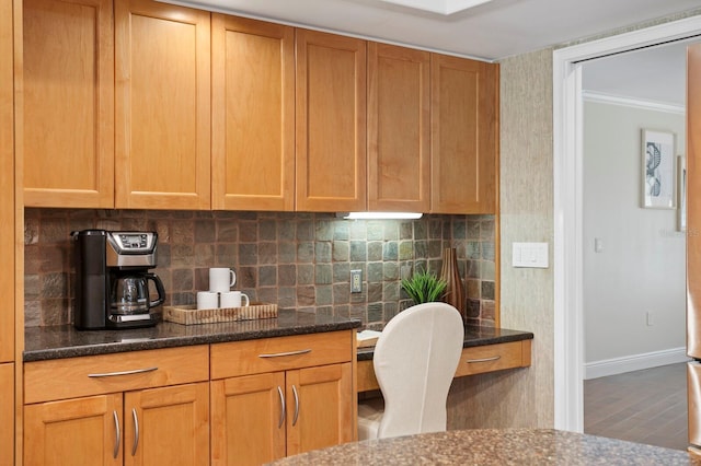 kitchen featuring decorative backsplash, built in study area, dark stone countertops, wood finished floors, and baseboards