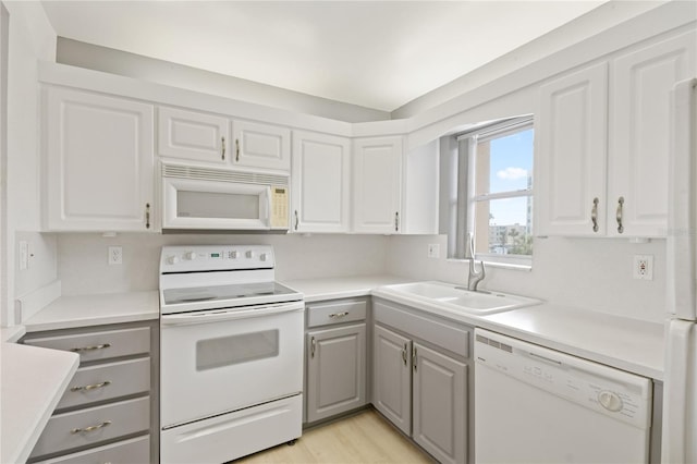 kitchen featuring a sink, light countertops, white appliances, and gray cabinets