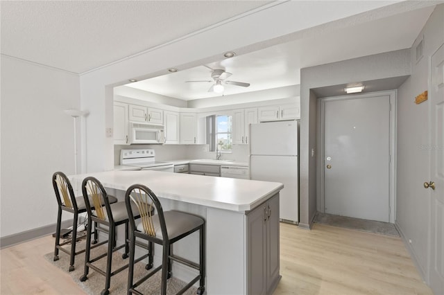 kitchen with a breakfast bar area, light countertops, light wood-style floors, white appliances, and a peninsula