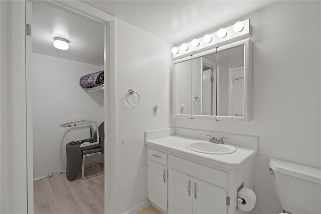 half bath with toilet, baseboards, wood finished floors, and vanity