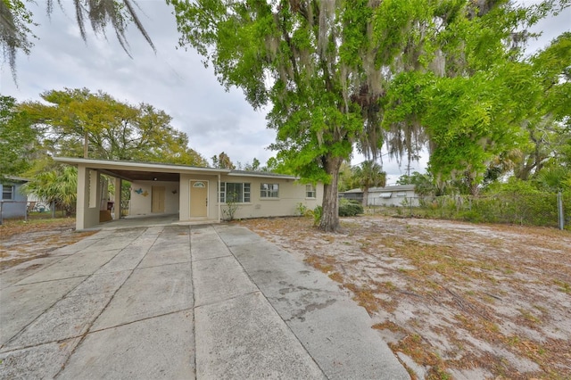 view of front facade with stucco siding, an attached carport, driveway, and fence