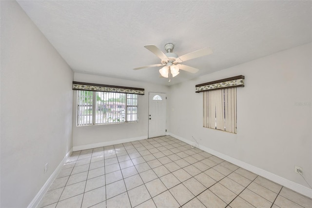 spare room with light tile patterned floors, a ceiling fan, baseboards, and a textured ceiling