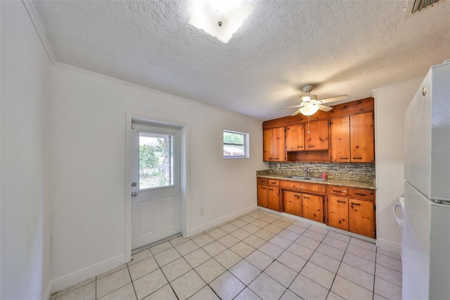 kitchen with brown cabinetry, baseboards, light tile patterned flooring, a sink, and backsplash