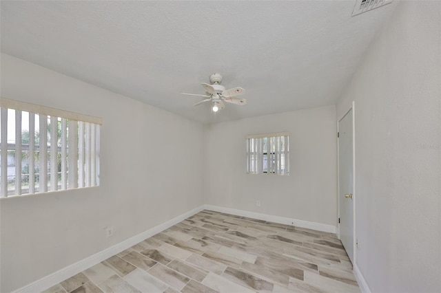 unfurnished room with a wealth of natural light, visible vents, a ceiling fan, and baseboards