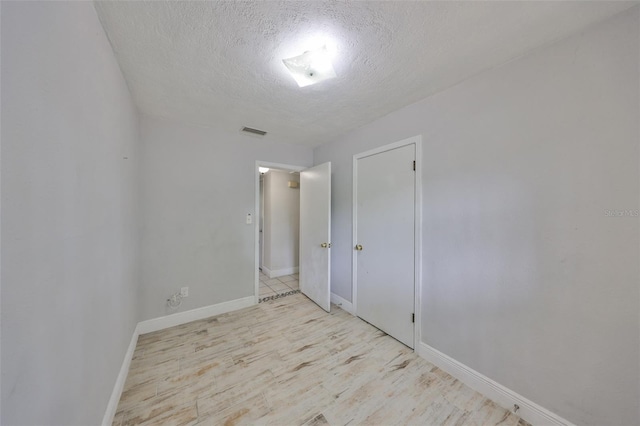 spare room with light wood-style floors, visible vents, baseboards, and a textured ceiling