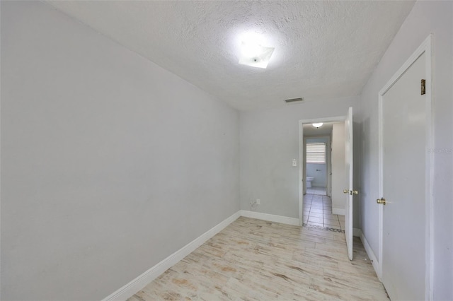 spare room with visible vents, a textured ceiling, light wood-style floors, and baseboards