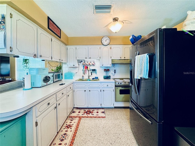 kitchen with visible vents, white range with electric cooktop, freestanding refrigerator, light countertops, and a sink