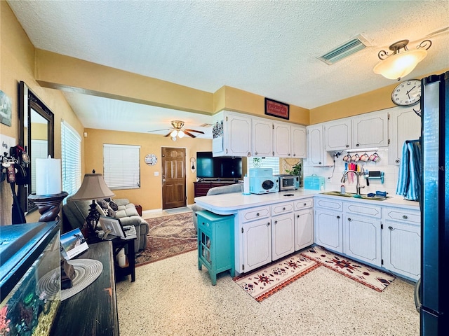 kitchen with a sink, visible vents, white cabinets, open floor plan, and light countertops