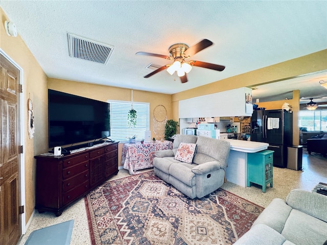 living room featuring light speckled floor, visible vents, ceiling fan, and a textured ceiling