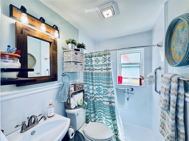 full bathroom featuring toilet, a shower with curtain, a sink, and a wainscoted wall