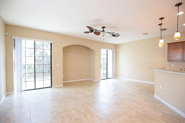 empty room featuring baseboards, visible vents, arched walkways, and a ceiling fan