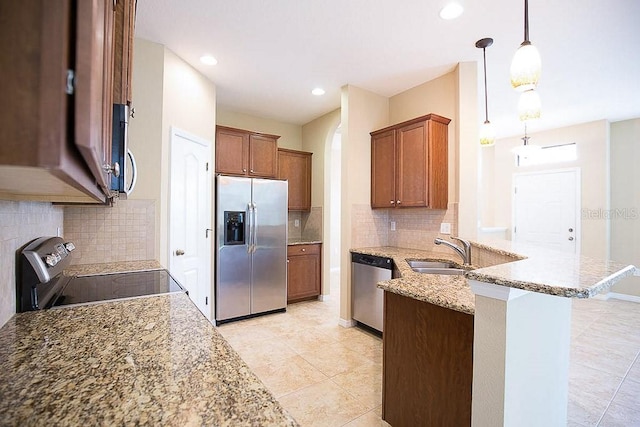 kitchen featuring brown cabinets, stainless steel appliances, a sink, light stone countertops, and a peninsula