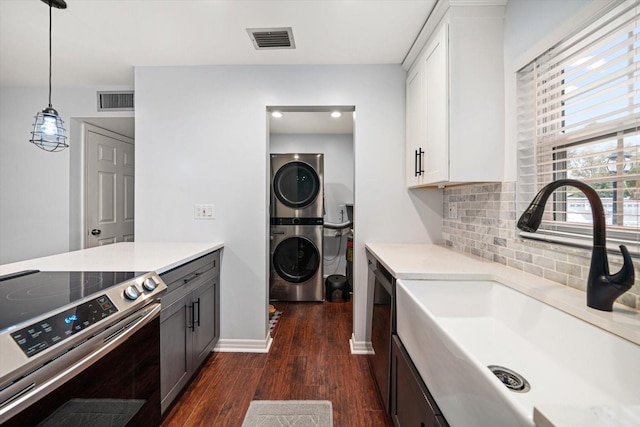 kitchen featuring visible vents, dark wood-type flooring, stacked washer / drying machine, stainless steel appliances, and a sink