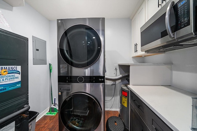 laundry area featuring stacked washer and dryer, dark wood-type flooring, laundry area, baseboards, and electric panel