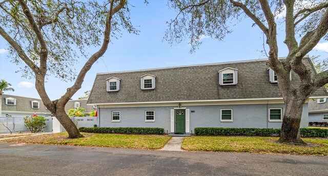 townhome / multi-family property with mansard roof, roof with shingles, fence, and stucco siding