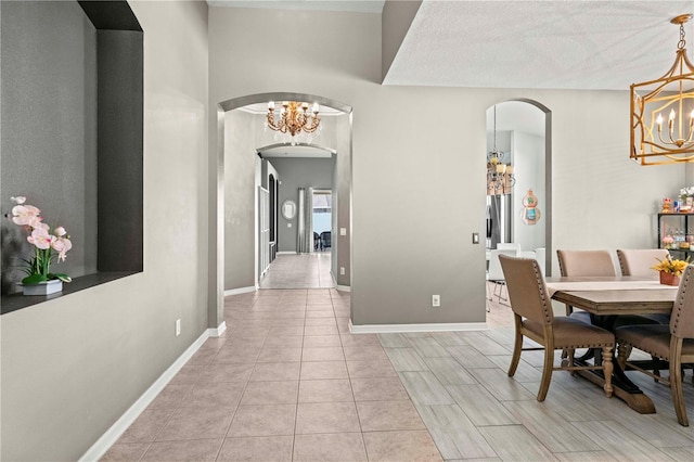 dining space featuring arched walkways, a notable chandelier, baseboards, and light tile patterned floors