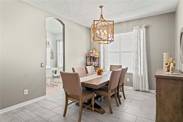 dining room with arched walkways, baseboards, a chandelier, and a healthy amount of sunlight