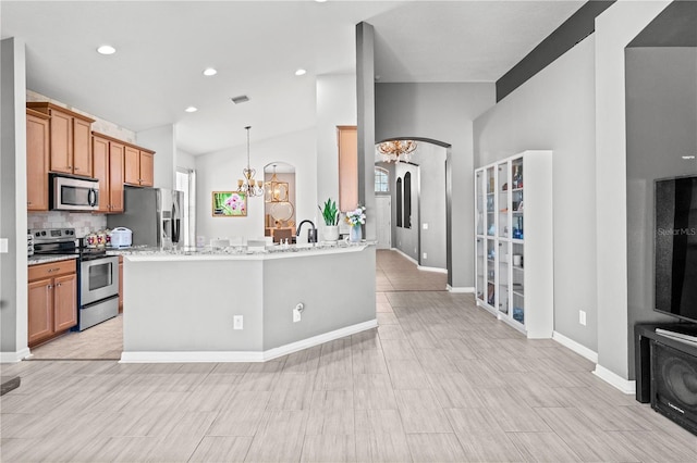 kitchen featuring brown cabinetry, decorative backsplash, lofted ceiling, appliances with stainless steel finishes, and a notable chandelier