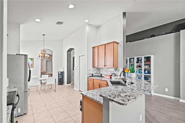 kitchen featuring light stone counters, a peninsula, a sink, appliances with stainless steel finishes, and tasteful backsplash