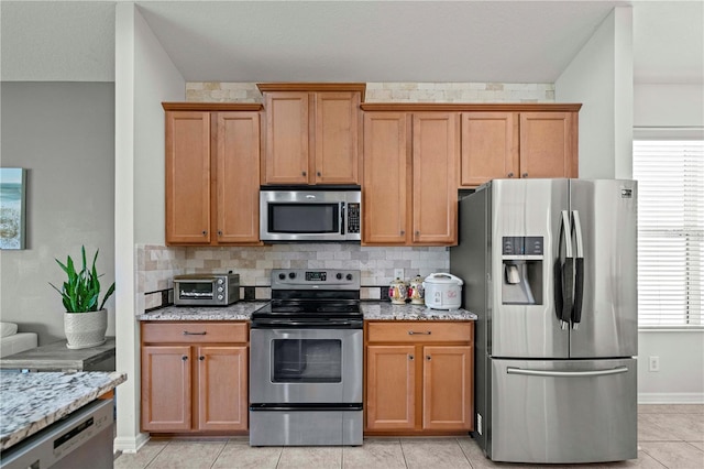 kitchen featuring stainless steel appliances, tasteful backsplash, and light stone countertops