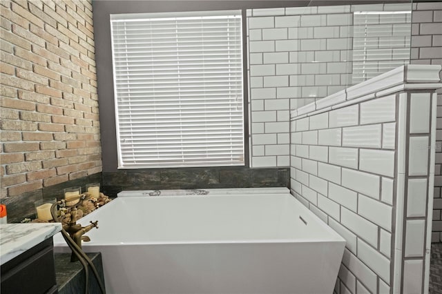 bathroom featuring a freestanding tub, vanity, and brick wall